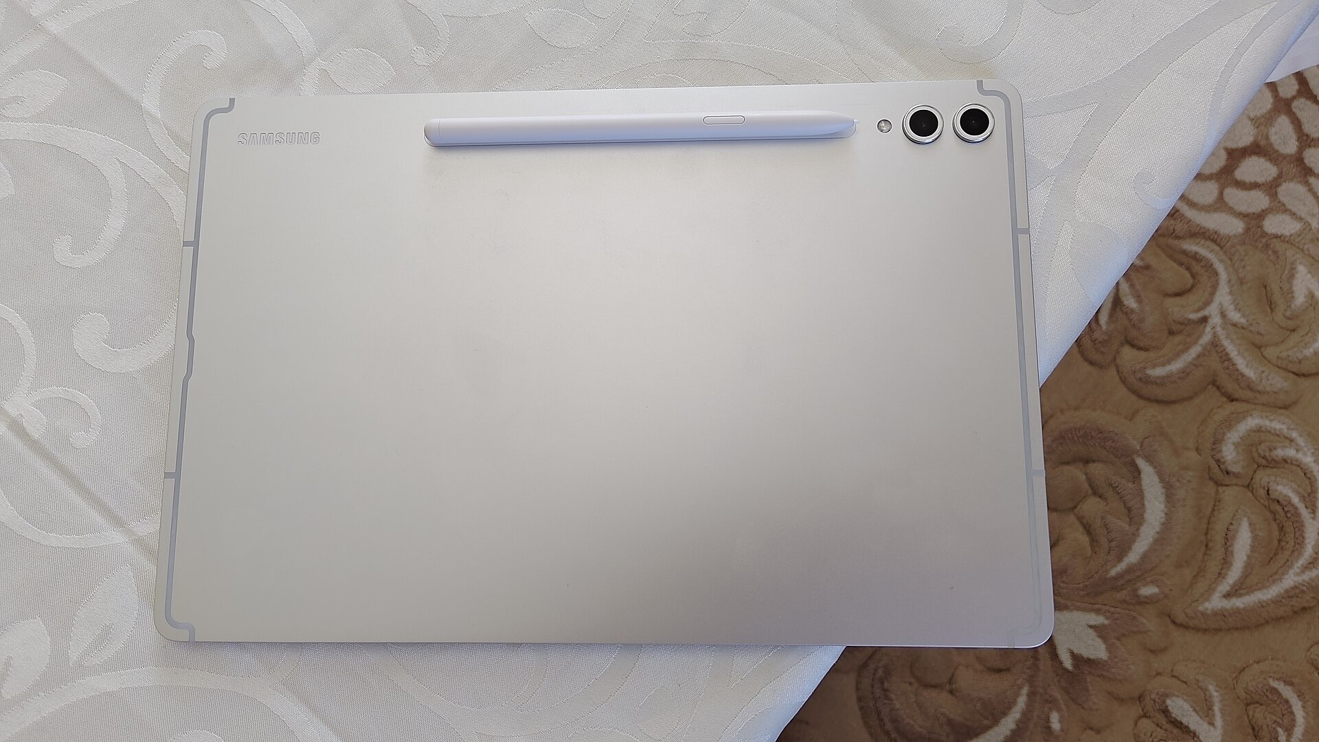 A Platinum Silver Samsung Galaxy Tab S10+ resting on a table face down with the bundled S Pen charging. (Samsung Galaxy Tab S10)